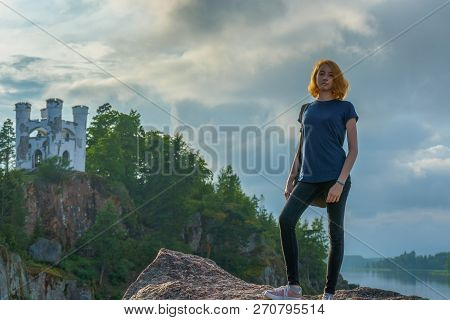 Pretty Young Lady With Red Hair Standing On Stone Near Bay Shore In Summer Evening. Tourist On The B