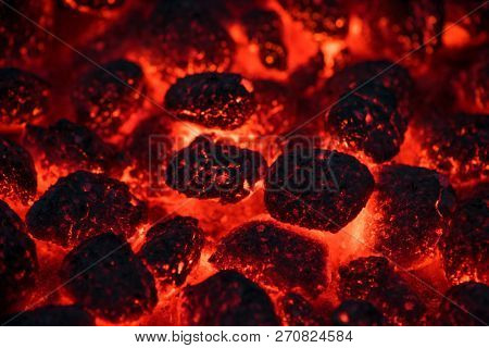 Coals smolder and glow. Residual flame from smoldering coals in cinder, closeup view. Flicker of burning coals at night.