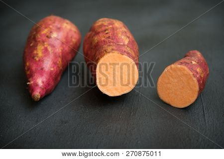 Raw orange sweet potatoes close up on dark background. 