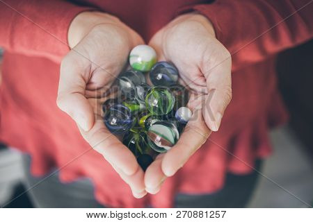 Marbles In Hand. Colorful Glass Marbles As Background. Childhood Games. Close Up View Of Girl Hand F