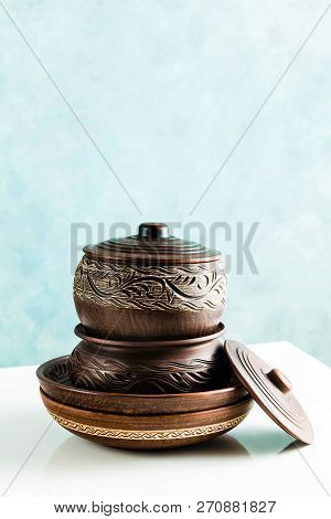 Pots And Plates Of Clay On A White Table And A Blue Background. Clay Pottery Kitchen Utensils Made B