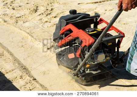 Builder With Vibratory Plates Seals The Base Sand For Pouring Concrete.