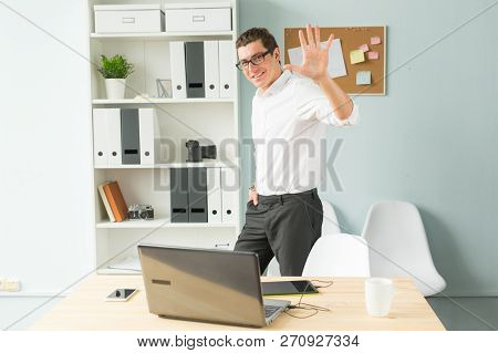 Business, Office, People Concept - Handsome Man In Glasses Stands In The Office Near A Computer And 