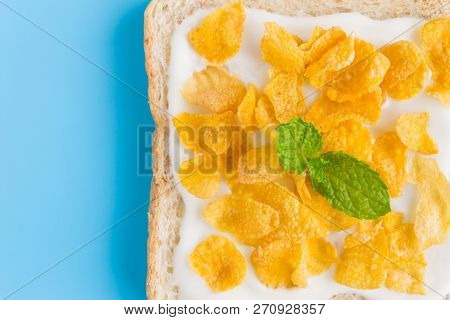 Cornflakes On Yogurt On Bread With Peppermint On Blue Pastel Background Flatlay Close Up. Cereal Bre
