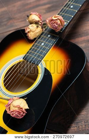 Acoustic Guitar With Dried Roses On The Wooden Table. Template For Advertising A Concert Of Memory O
