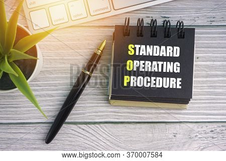 Standard Operating Procedure Text With Fountain Pen, Decorative Plant, Keyboard And Notepad On Woode