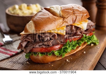 Roast Beef Submarine Sandwich With Cheese, Tomato And Lettuce On A Wooden Cutting Board