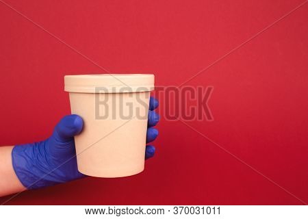 Courier Hand In Blue Disposable Protective Gloves On Burgundy Red Background Holding Round Paper Foo