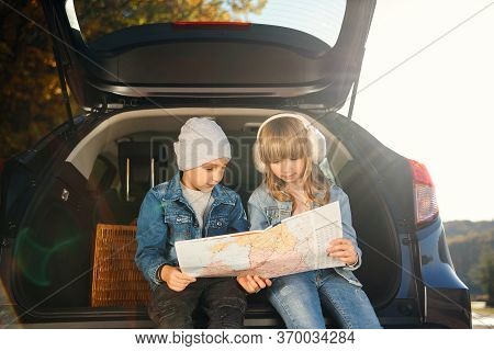 Agreeable Boy And Girl Are Looking At The Road Map While Sitting In The Autos Trunk And Discussing T