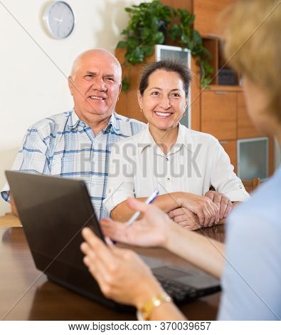 Aged Smiling Couple Talking With Employee With Laptop At Home. Focus On Woman.
