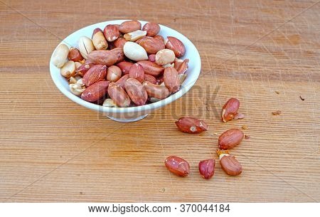 Plateful Of Organic Unsalted Peanuts And Spilled Unsalted Peanuts On Wooden Background