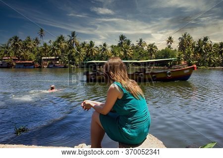 A Woman Sitting Enjoying The View Of Floating Houseboat In The Backwater Of Allepey And A Man Swimmi