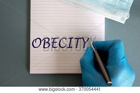 Covid-19 Pandemic Coronavirus Concept. Male Hand In Blue Glove Writes The Words 'obecity' On A White