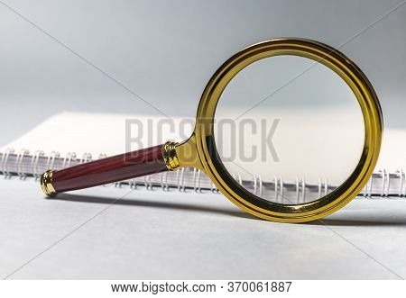 Close Up Golden Magnifying Glass Loupe With Red Wooden Handle On White Planner Or Notebook And Gray 