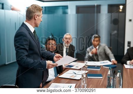 Confident Mature Businessman In Formal Wear Holding Some Documet And Discussing Something With Multi