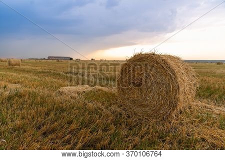 Haystack Rolled Up On A Field Landscape, Sunset Stormy Sky