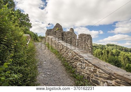 Ascent To A Castle Ruin On A Hill On A Path Along A Wall On A Cloudy Summer Day.