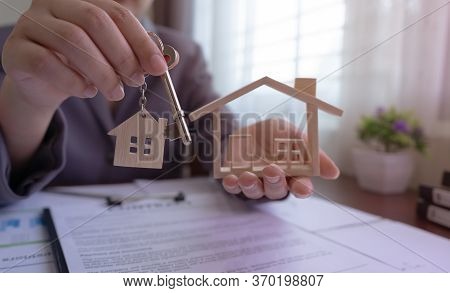 Close Up. Real Estate Agent Holding House Key And House Model On Table With House Designs Document, 