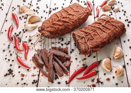 Beef jerky, bresaola, dried beef - Basturma in Red Pepper with black pepper peas, chilli and garlic on a light wooden background. Armenian national snack and dishes of Russian national cuisine 