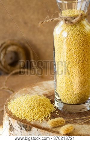 Millet In A Glass Jar On A Wooden Stand, Next Is An Ear Of Wheat, On A Beige Background