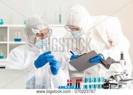 Scientist examine vaccine testing of coronavirus covid-19 pandemic in science lab. Scientist wear PPE personal protective suits and medical goggles. Medical Science technology and healthcare concept.