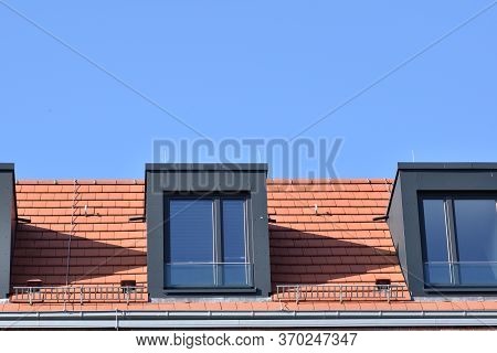 Red Roof Tiles And Dark Windows Against A Blue Sky