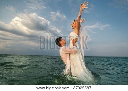 浪漫的新婚夫妇享受暑假。年轻的新郎在海中解除他的新娘