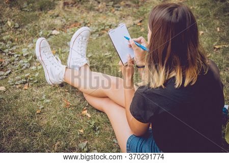 Girl Writing In Notebook On The Green Grass Background