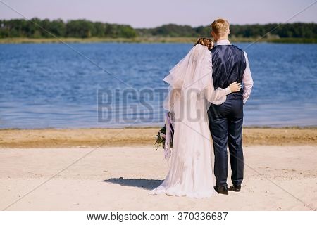 Just Married Couple Standing In Nature Holding Hands And Looking At Beautiful View Of River. Enjoyin