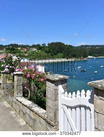 Small Fishing Village With Boats And Beach. View With White Wooden Door And Flowers. Redes, Galicia,