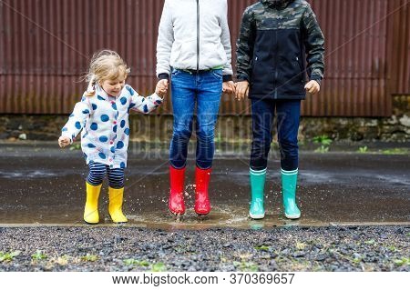 Three Children, Toddler Girl And Two Kids Boys Wearing Red, Yellow And Green Rain Boots And Walking 