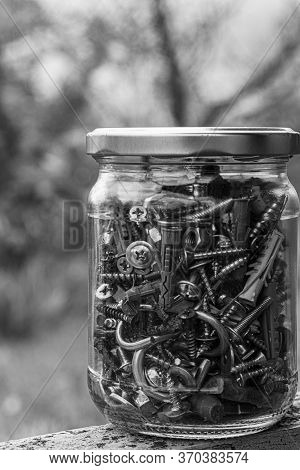 Black And White Photo Of Glass Jar Of Assorted Hardware Bolts And Nuts Closeup Through Blurry Glass 