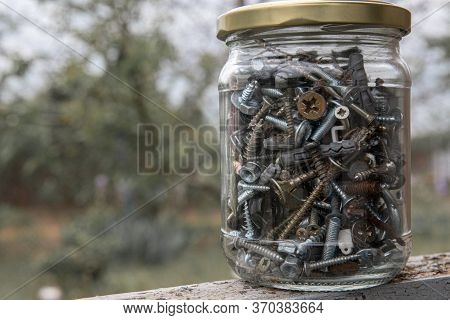 Closeup Of Glass Jar Of Assorted Hardware Bolts And Nuts Shot Through Blurry Glass On Bokeh Backgrou