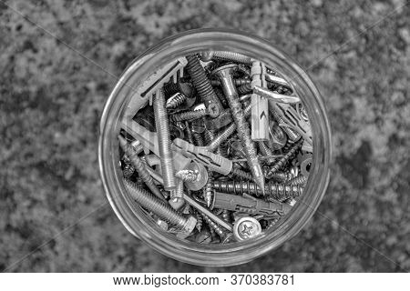 Black And White Photo Of Assorted Hardware Bolts And Nuts In Glass Jar With Blurry Grunge Stone Back