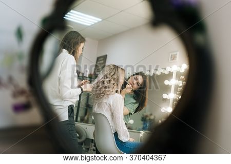 Two Professional Female Make-up Artist Doing Makeover In Lighting Dressing Room, View From Afar. Con