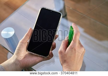 Woman Is Cleaning A Smartphone With A Jet Of Alcohol Aerosol Hand Sanitizer And Disposable Cloth At