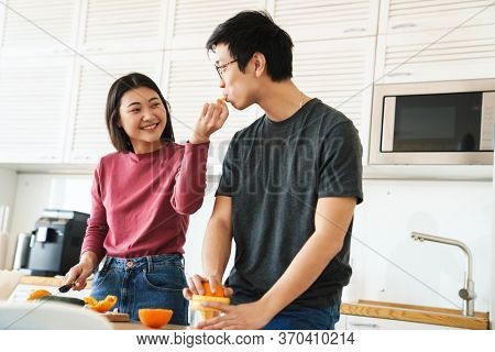 Lovely youg asian couple cooking breakfast together in the kitchen, squeezing oranges for juice