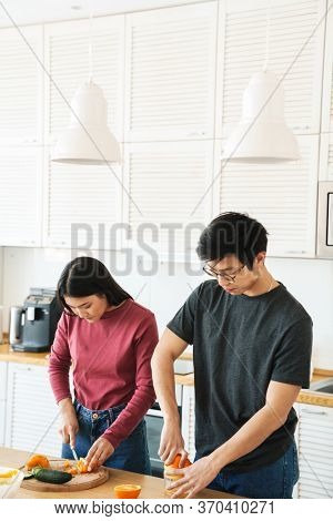 Lovely youg asian couple cooking breakfast together in the kitchen, squeezing oranges for juice