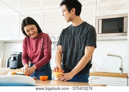 Lovely youg asian couple cooking breakfast together in the kitchen, squeezing oranges for juice