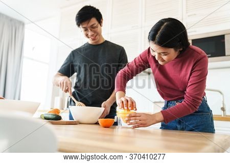 Lovely youg asian couple cooking breakfast together in the kitchen, squeezing oranges for juice