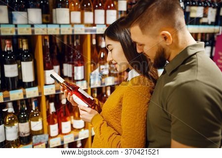 Cheerful couple choosing alcohol in supermarke