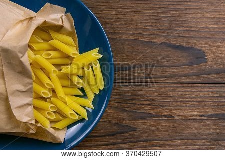 Pene Lisce Pasta In A Craft Paper Bag On A Blue Plate On A Wooden Table. Top Views With Clear Space.