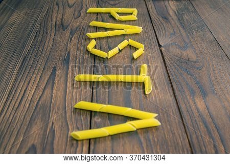 The Word Pasta Is Made From Pasta Pene Lisce On A Wooden Table. Front Views.