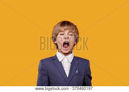 Little Boy In A White Shirt And Gray Jacket Tired And Yawning.