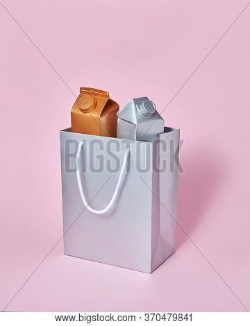 Two mock-up packages for dairy products golden and silver in a paper silver bag on a pastel pink background with soft shadows, copy space. Eco friendly concept. Recycling concept.