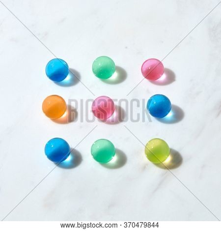 Colorful hydrogel balls with crystal lquid as a square pattern on a grey marble table with shadows and reflections, copy space. Top view.