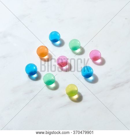 Hydrogel balls with crystal colorful lquid inside as a diagonal pattern on a grey marble table with hard shadows and reflections, copy space. Top view.