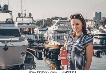 Cute Girl In A Striped Dress Makes Selfie On A Camera Of Her Red Smartphone With Selfie Stick On The
