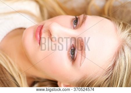 Close-up Of Young Charming Woman Laying With Painted Shape For Eyebrows. Blonde Lady At Cosmetologis