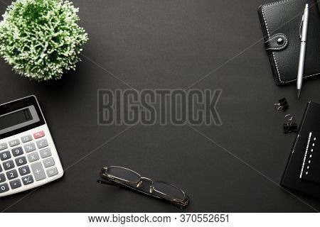 Top view of analyzing black office desk with calc, notebook, pen and a lot of things. Flat lay table layout. Copy space for text.